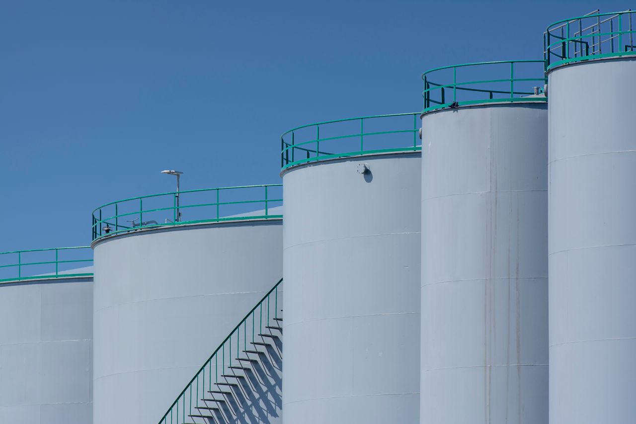 Home Large industrial storage tanks with green railings against a clear blue sky.